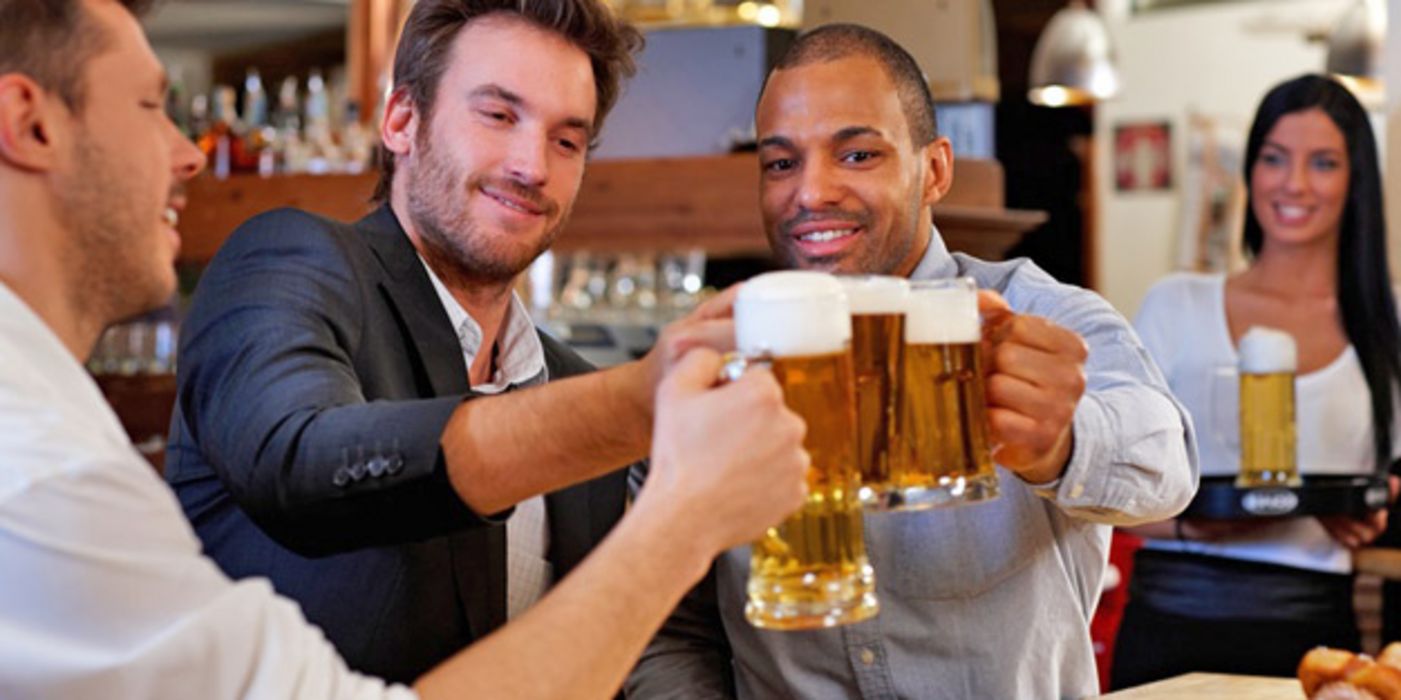 Drei jüngere Männer stoßen in einer Kneipe mit Bierhumpen an