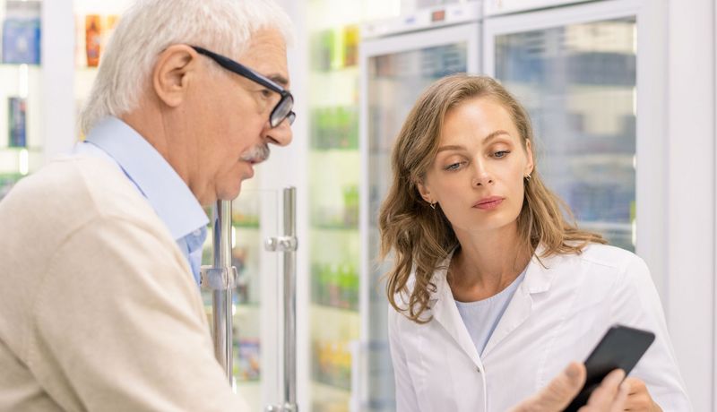 Älterer Mann zeigt einer Apothekerin sein Smartphone.