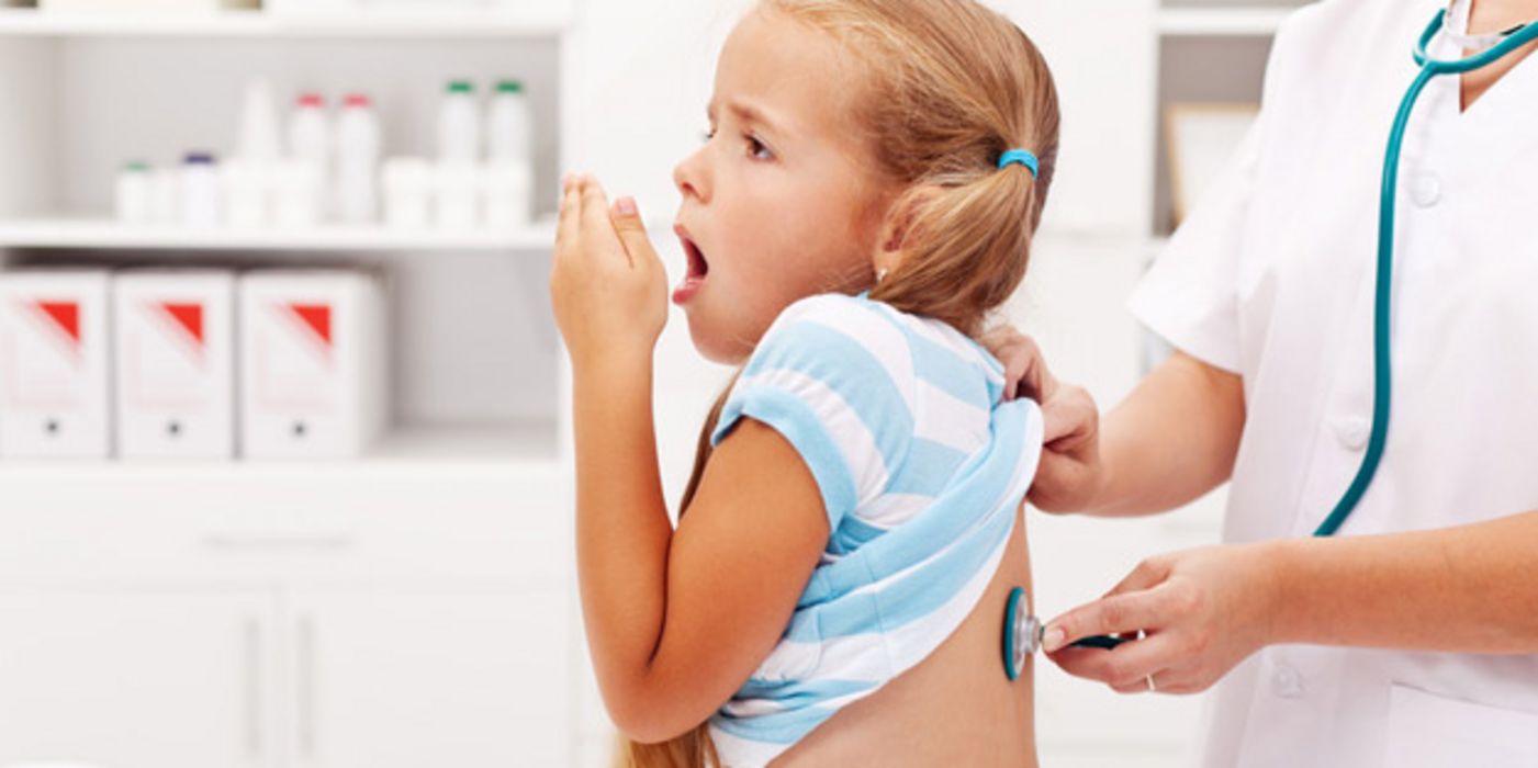 Mädchen im Grundschulalter bekommt beim Arzt den Rücken mit Stethoskop abgehorcht während sie hustet