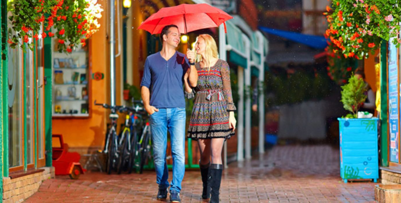 Vergnügtes Paar (Frau und Mann) nachts in der Stadt im Sommerregen unter pinkem Regenschirm