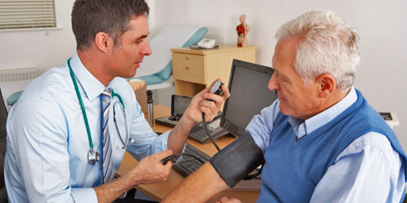 Junger Arzt misst bei älterem Patienten den Blutdruck