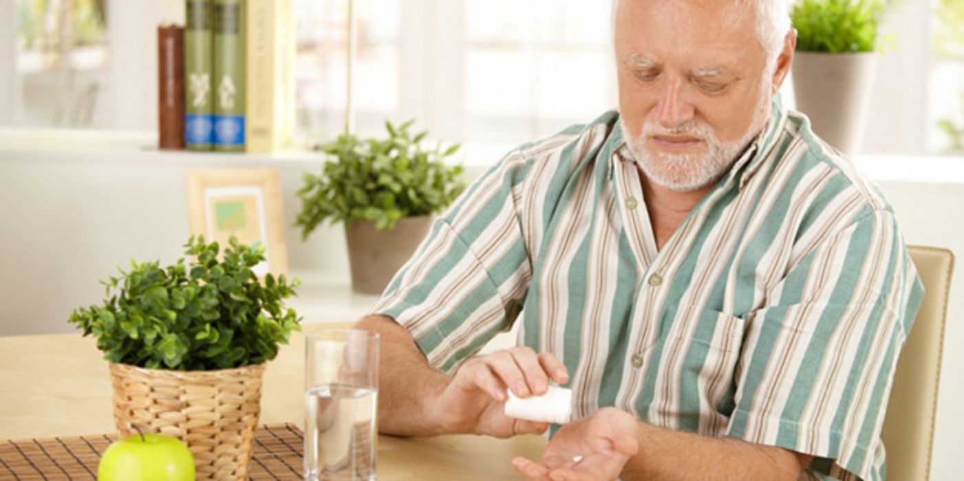 Älterer Mann nimmt ein Medikament ein, am Tisch sitzend
