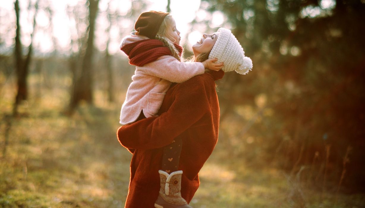 Mutter, hat Tochter auf dem Arm, draußen im Wald.