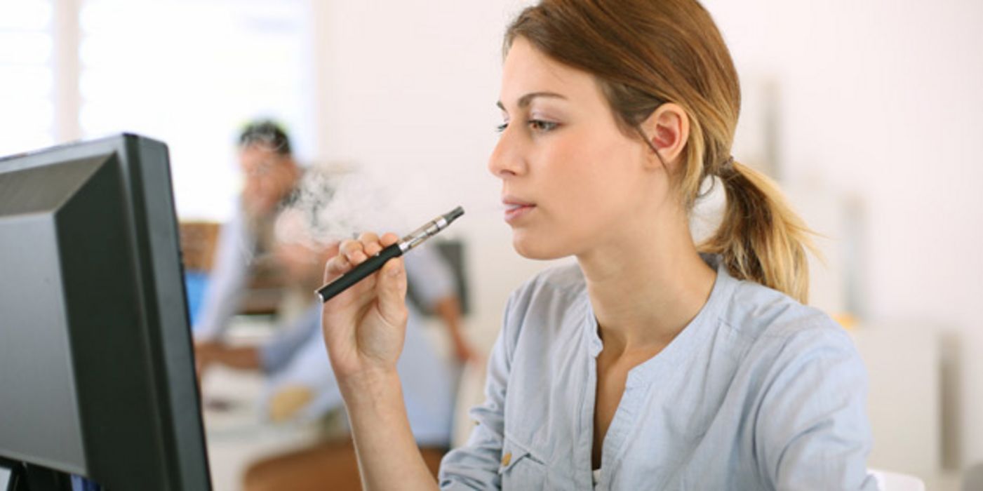 Im Büro: Jüngere Frau vor Bildschirm, E-Zigarette in einer Hand