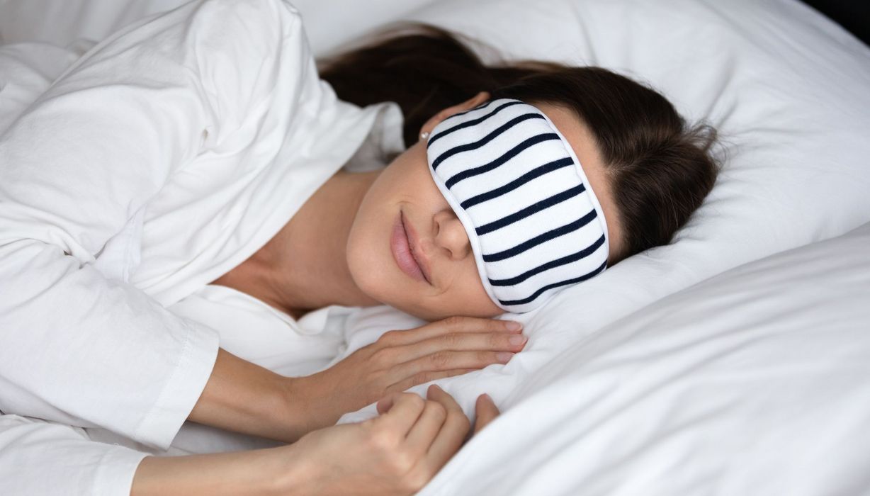 Junge Frau mit Schlafmaske im Bett.