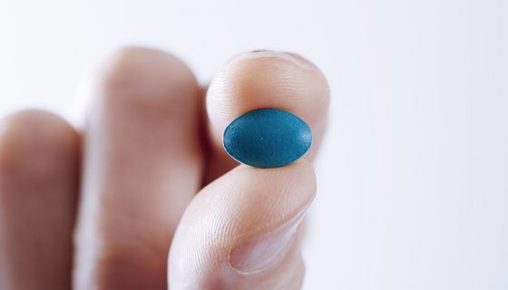 Eine Hand hält eine blaue, rautenförmige Tablette in die Kamera.