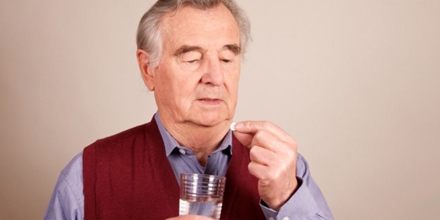 Senior nimmt eine Tablette mit einem Glas Wasser ein