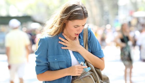 Junge Frau hat Atemprobleme, aus ihrer Handtasche zieht sie einen Inhalator.