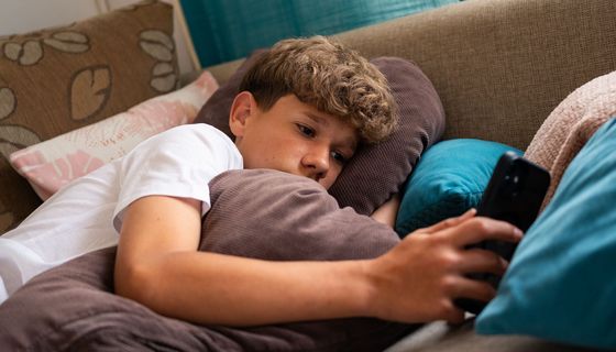 Unglücklicher Jugendlicher liegt auf einem Sofa, das Handy in der Hand.