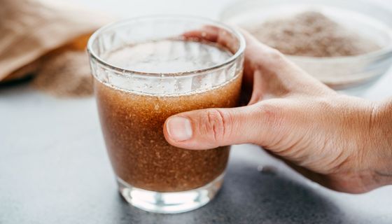Eine Hand hält ein Glas mit in Wasser eingeweichten Flohsamen.
