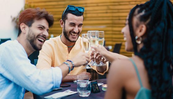 Junge, gutgelaunte Menschen stoßen mit einem Glas Sekt an.
