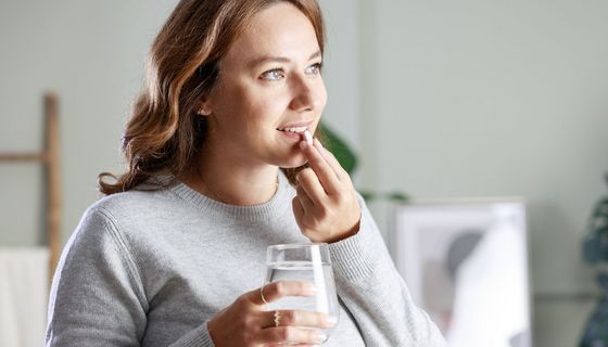 Eine Frau, etwa 30 Jahre alt, nimmt eine Tablette ein.