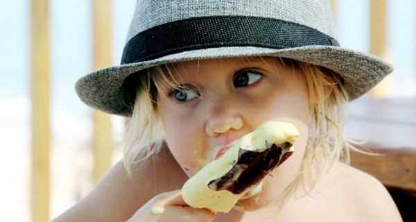 Ein kleines Mädchen mit Hut isst ein Eis.