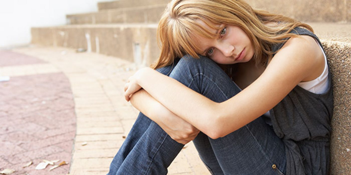 Traurige junge Frau (um die 20), blond auf dem Boden sitzend, an Treppenstufe gelehnt, Kopf auf angezogenen Knien