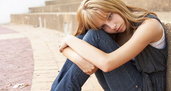 Traurige junge Frau (um die 20), blond auf dem Boden sitzend, an Treppenstufe gelehnt, Kopf auf angezogenen Knien