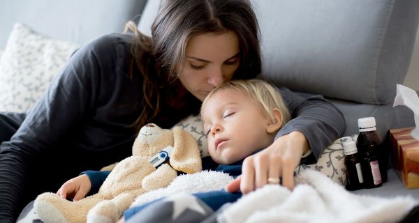 Mutter, liegt mit krankem Kind im Bett und umarmt es.