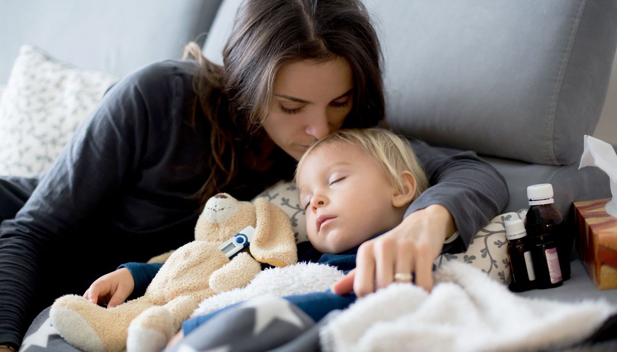 Mutter, liegt mit krankem Kind im Bett und umarmt es.