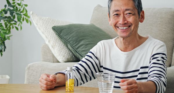 Älterer Mann mit einer Packung Tabletten und einem Glas Wasser, lächelt in die Kamera.