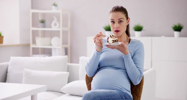 Eine schwangere Frau schaut erstaunt, in der Hand ein Tellerchen mit einem Stück Kuchen darauf.