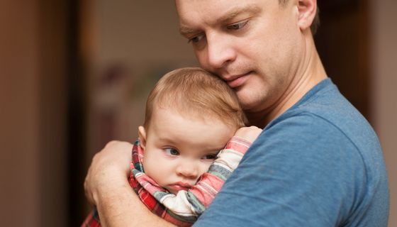 Vater hält sein Baby im Arm. Beide blicken nachdenklich.