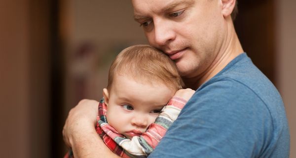 Vater hält sein Baby im Arm. Beide blicken nachdenklich.