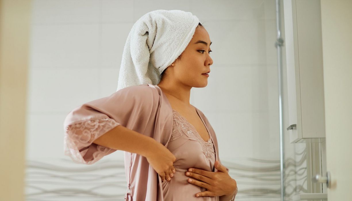 Junge Frau tastet sich im Badezimmer die Brust ab.