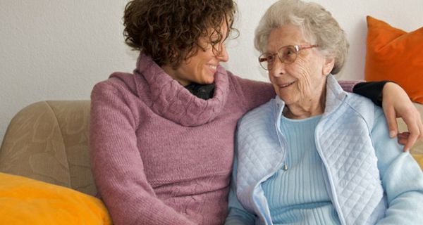 Seniorin und junge Frau sitzen nebeneinander auf einer Couch