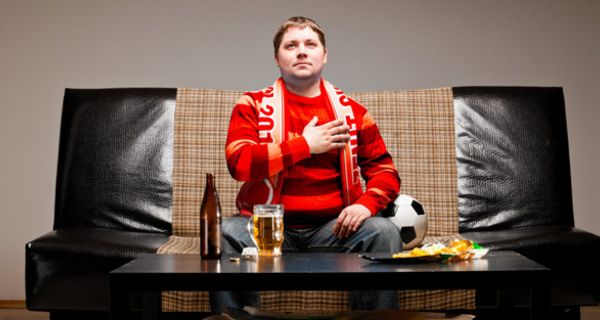 Mann mit Fanschal und Bierflasche auf dem Sofa.