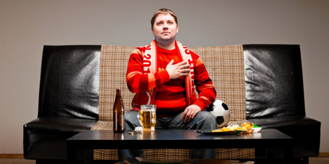 Mann mit Fanschal und Bierflasche auf dem Sofa.