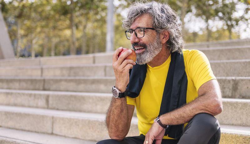 Entspannter älterer Mann beißt in einen Apfel.