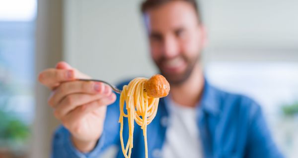 Mann, hält eine Gabel mit Nudeln und Wurst in die Kamera.