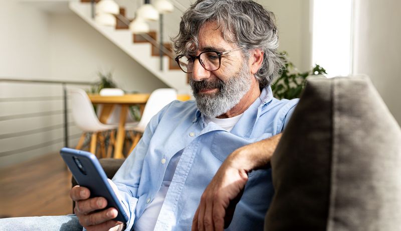 Erwachsener Mann mit Handy in der Hand auf Sofa sitzend