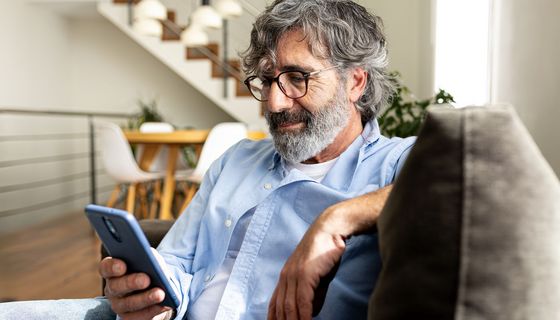 Erwachsener Mann mit Handy in der Hand auf Sofa sitzend