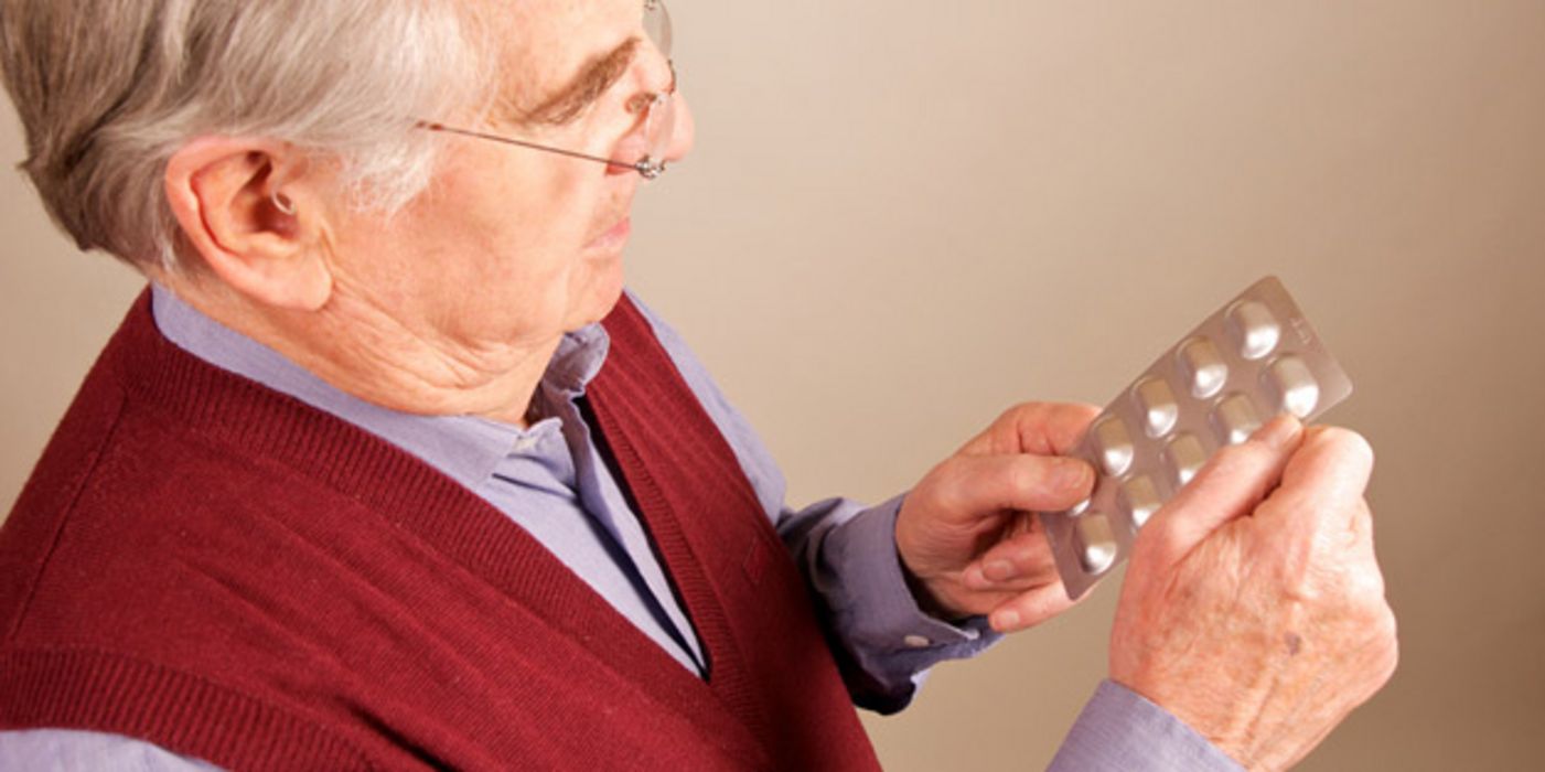 Älterer Mann mit Blisterpackung schaut auf Blisterpackung mit Antibiotika in seinen Händen