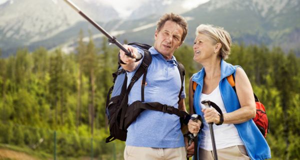 Paar, ca. Mitte 50, in den Bergen beim Wandern, Mann deutet mit Wanderstock in die Ferne