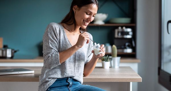 Junge Frau, sitzt in der Küche und isst Joghurt.