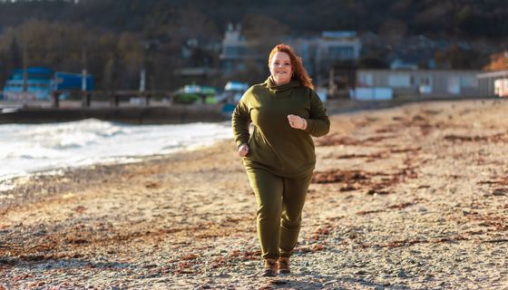Übergewichtige Frau, joggt am Strand.