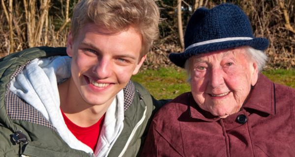 Portraitfoto Oma (über 90) und Enkel in der Natur, Oma in Hut und Mantel, Enkel in T-Shirt Shirt und Blouson