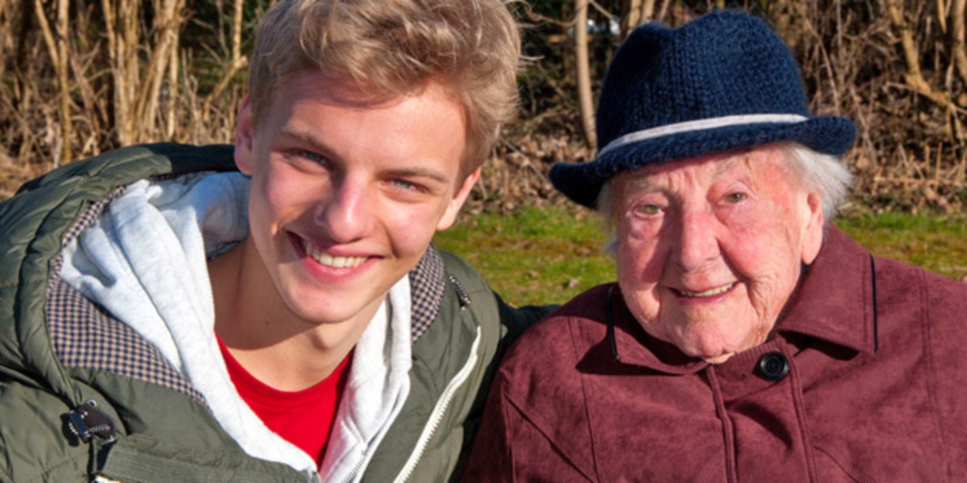Portraitfoto Oma (über 90) und Enkel in der Natur, Oma in Hut und Mantel, Enkel in T-Shirt Shirt und Blouson