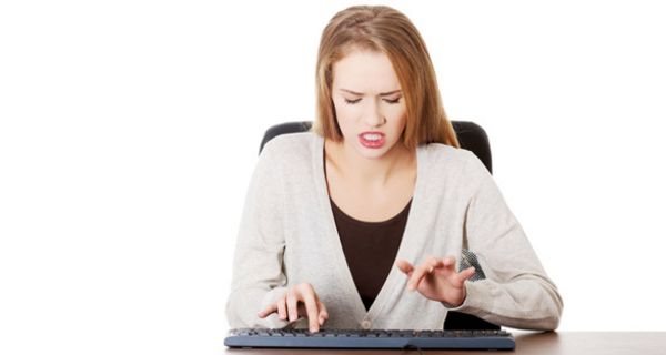 Junge Frau schaut wütend auf PC-Tastatur und hackt darauf herum