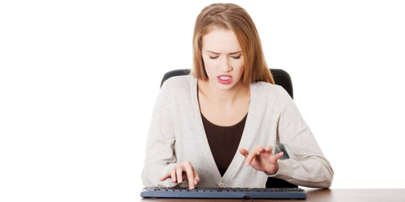 Junge Frau schaut wütend auf PC-Tastatur und hackt darauf herum