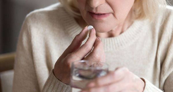 Ältere Frau, nimmt Tablette mit einem Schluck Wasser.