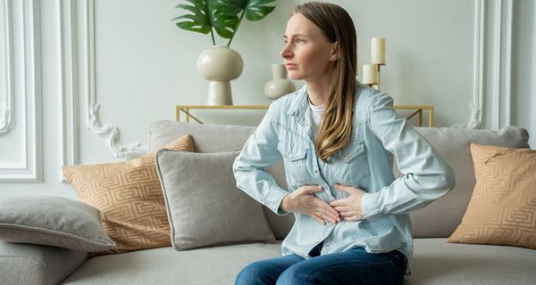 Junge Frau sitzt auf dem Sofa und hält sich den Bauch.