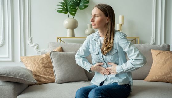 Junge Frau sitzt auf dem Sofa und hält sich den Bauch.