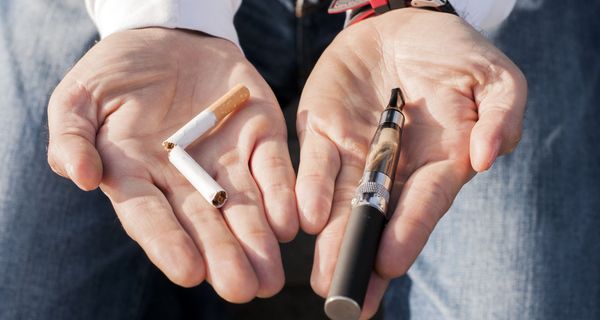 Mann, hält eine durchgebrochene Zigarette und eine E-Zigarette in der Hand.