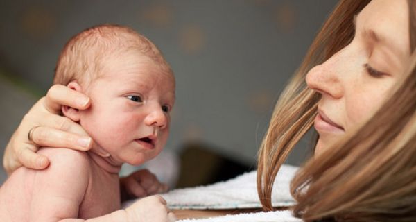 Frisch gebackene Mutter hält ihr Neugeborenes vor sich in Augenhöhe