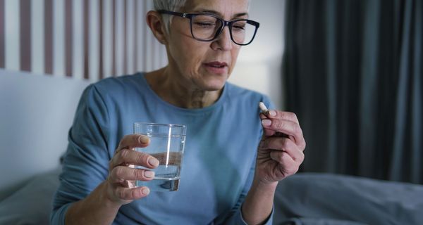 Seniorin nimmt Tablette mit einem Glas Wasser.