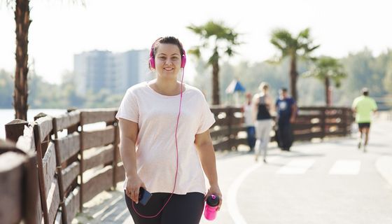 Frau mit Sportbekleidung mit Kopfhörern, übergewichtig.