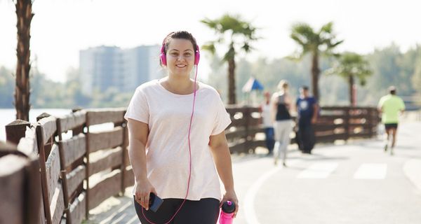 Frau mit Sportbekleidung mit Kopfhörern, übergewichtig.