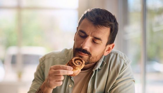 Mann riecht mit geschlossenen Augen an einem Zimtwirbel-Muffin.